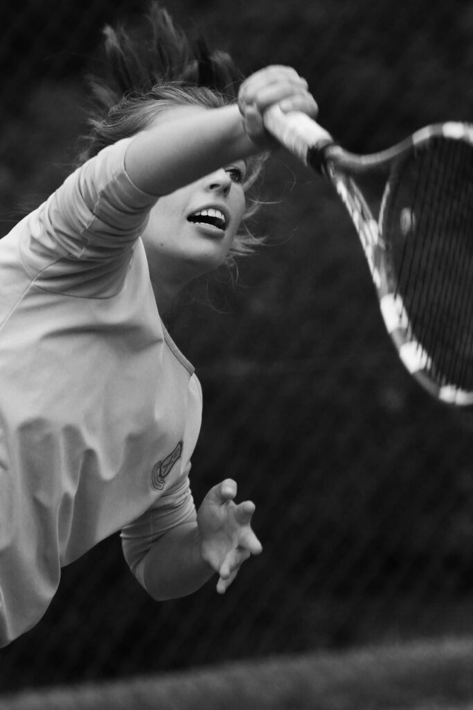 Black and white image of a woman serving in a tennis match, showing intense concentration.